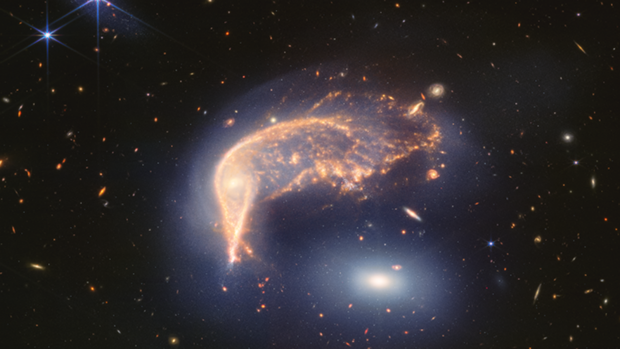  A dark background of space has a shining galaxy view in front of it, sort of shaped like a penguin. There's a glowing white orb toward the bottom right, representing the "egg" galaxy. 