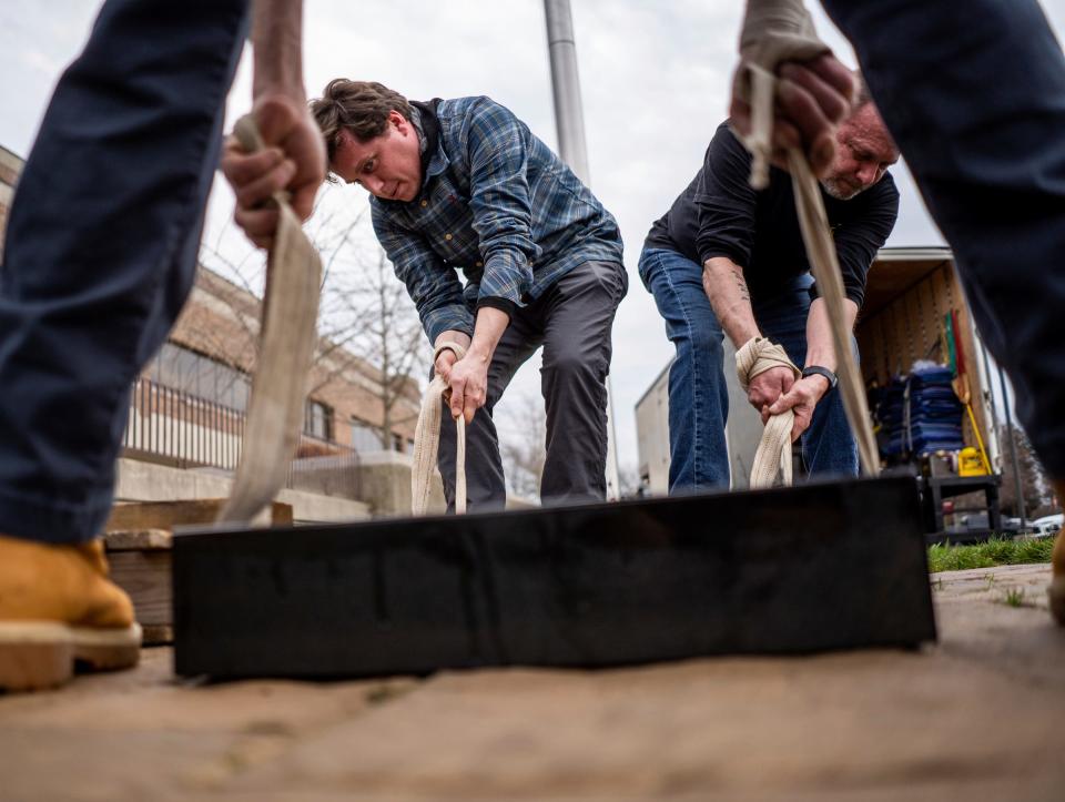 J. Noseda &amp; Son Inc. owners John Noseda, right, and his son Jake Noseda, left, pull straps with the help of Ken Nosada, foreground, as they work to place a granite base for the Southfield Police Department's &quot;Fallen Hero&quot; sculpture in a new location on Wednesday, April 5, 2023.