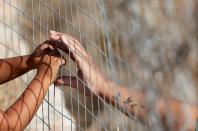 FILE PHOTO: Woman touches hands of a child through a fence at a new temporary camp for migrants and refugees on the island of Lesbos