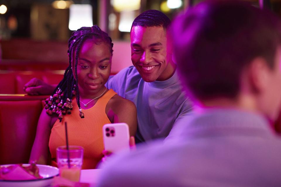 smiling man taking selfie with woman on smart phone by male friend