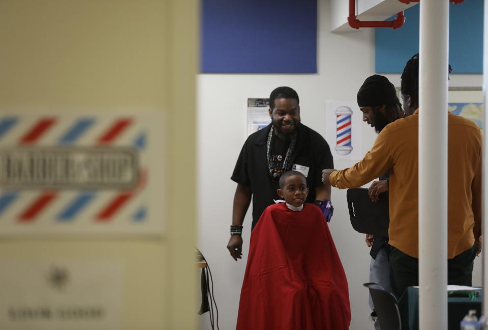 Barbers, Carl Williams, Roberto Murray and Devon Reynolds of Brothers & Sisters Unisex Salon, crowd around Kaylan Gastlon after his haircut and chat with him before he gets down from his chair. Reynolds is the owner of the salon that came to the school.