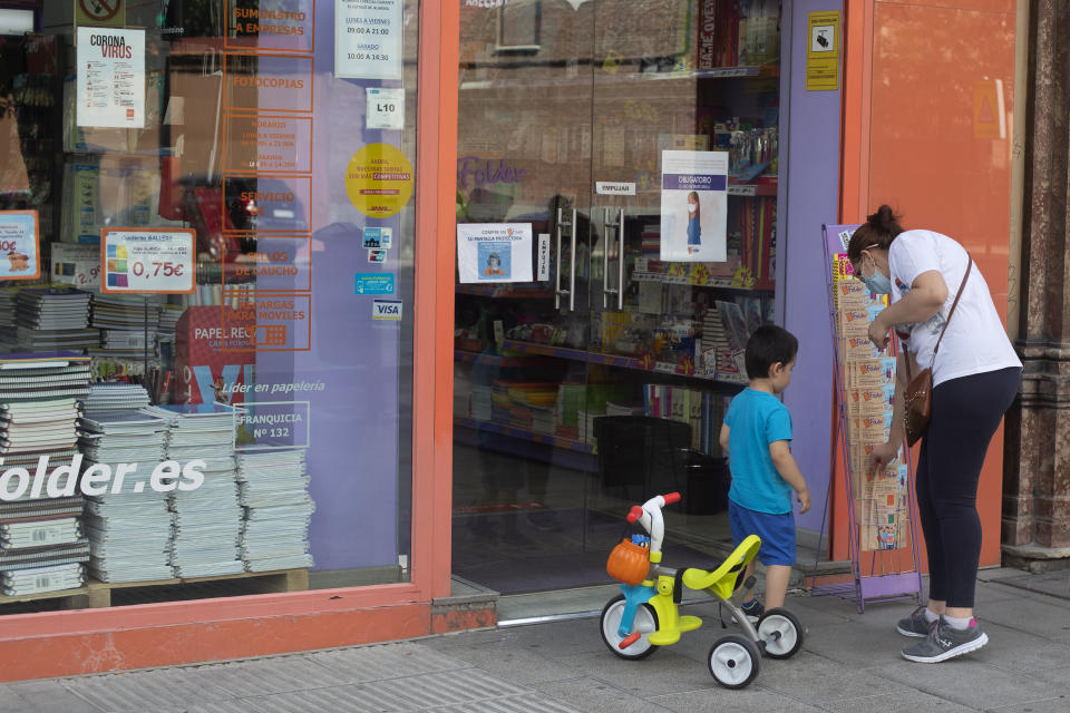 A woman and a young boy stop to pick up information leaflets at a store selling children's school stationery, backpacks, protective masks and hand sanitizers in Madrid, Spain, Monday, Aug. 24, 2020. Despite a spike in coronavirus infections, authorities in Europe are determined to send children back to school. Schools in the Spanish capital are scheduled to open on Sept. 4. (AP Photo/Paul White)