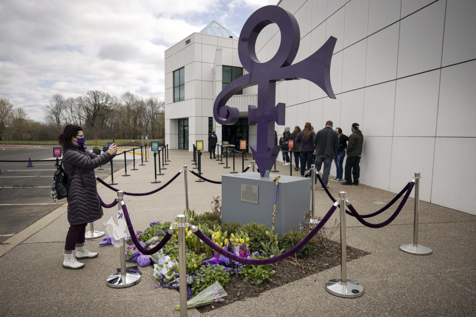 A fan takes a photo of a memorial, Wednesday, April 21, 2021, as others line up to go into Paisley Park in Chanhassen, Minn., on the fifth anniversary of Prince's death. Fans were allowed into the home and studio of the late musician 20 at a time to pay respect. (AP Photo/Stacy Bengs)