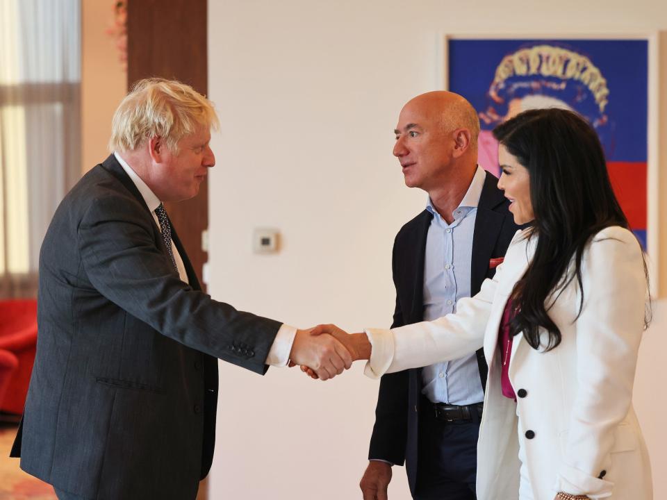 UK Prime Minister Boris Johnson (left) shakes hands with Jeff Bezos' girlfriend Lauren Sánchez while Jeff Bezos stands in the background.