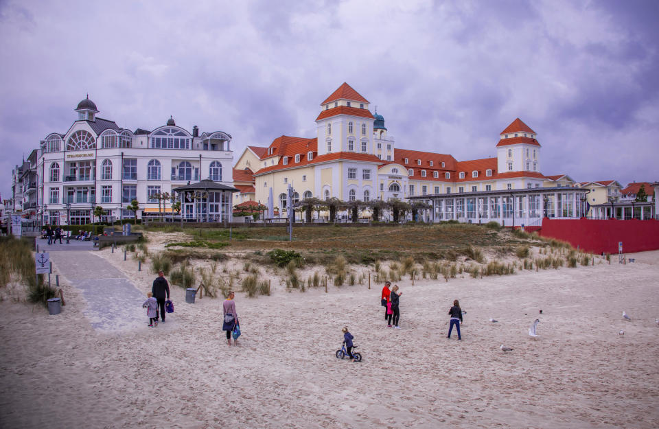 In this Saturday, May 23, 2020, some tourists stay on the beach in front of the Hotel Kurhaus Binz at the Baltic Sea island Ruegen in Binz, Germany. Germany's states, which determine their own coronavirus-related restrictions, have begun loosening lockdown rules to allow domestic tourists to return. ( Jens Buettner/dpa via AP)