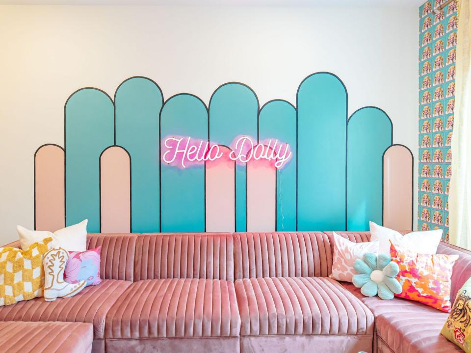 A mural that says "Hello Dolly" behind a pink couch.