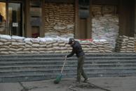 A woman cleans up rubbish in front of an entrance to a city administration building in Slovyansk , eastern Ukraine, Wednesday, April 16, 2014. Pro-Russian protesters fortified the entrance with sand bags. The city of Slovyansk has come under the increasing control of the pro-Russian gunmen who seized it last weekend. (AP Photo/Sergei Grits)