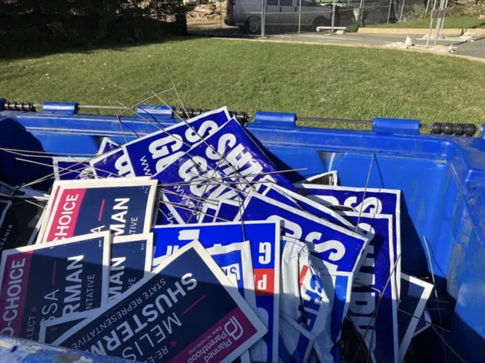 A large blue dumpster filled with democratic campaign signs