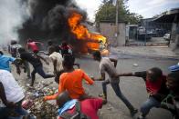 Demonstrators run away from police who are shooting in their direction, as a car burns during a protest demanding the resignation of Haitian President Jovenel Moise in Port-au-Prince, Haiti, Tuesday, Feb. 12, 2019. Protesters are angry about skyrocketing inflation and the government's failure to prosecute embezzlement from a multi-billion Venezuelan program that sent discounted oil to Haiti. (AP Photo/Dieu Nalio Chery)