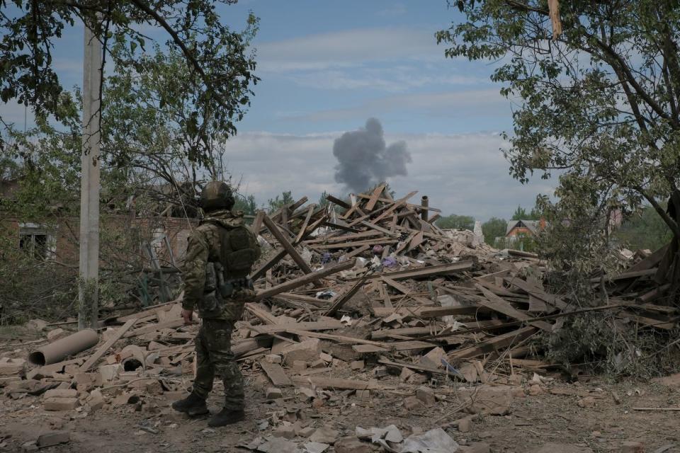 Police officer Oleksii Kharkivskyi looks at smoke rising from a Russian glide bomb impact site in Vovchansk, Kharkiv Oblast, on May 11, 2024. (Francis Farrell/The Kyiv Independent)