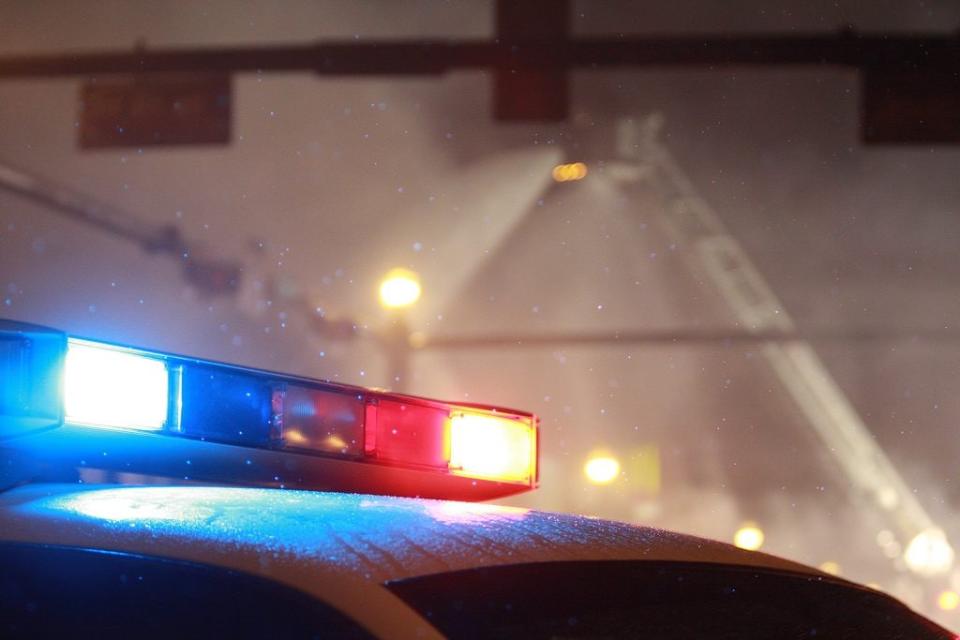 A lone police car stands guard as aerial and ground firemen battle a building fire in light snow. Credit: Getty