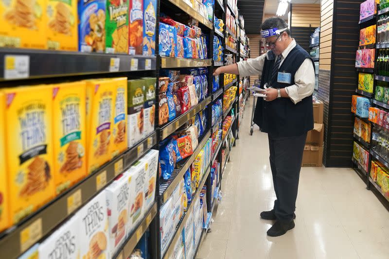FILE PHOTO: A worker with a face shield checks products on the shelf of a grocery store
