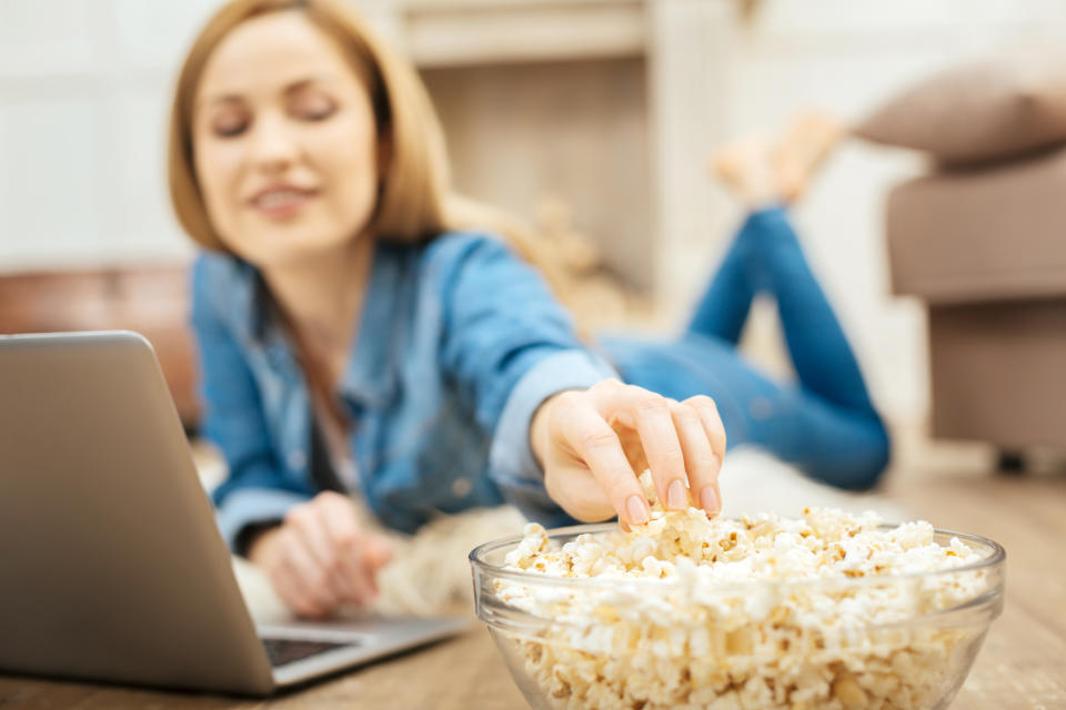 Woman eating popcorn on the floor while using a laptop.