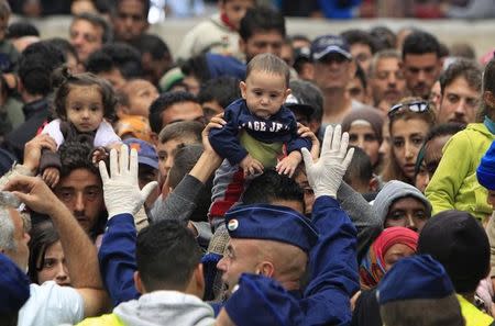 A migrant holds his baby as a policeman tries to maintain order at the Keleti station in Budapest, Hungary September 10, 2015. REUTERS/Bernadett Szabo