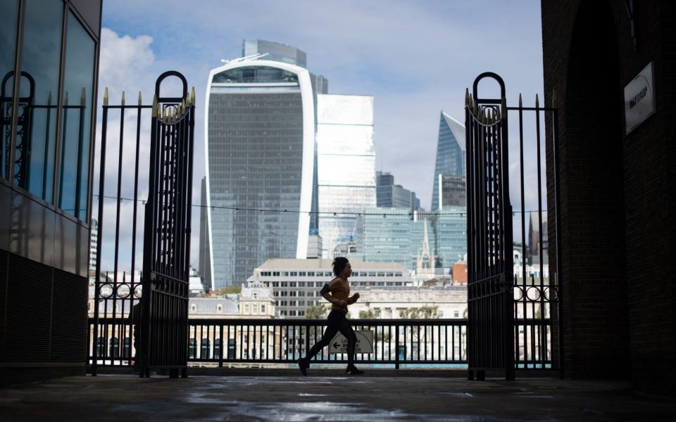 A jogger runs along the river Thames, passing skyscrapers in the City financial district of London - Dominic Lipinski /PA