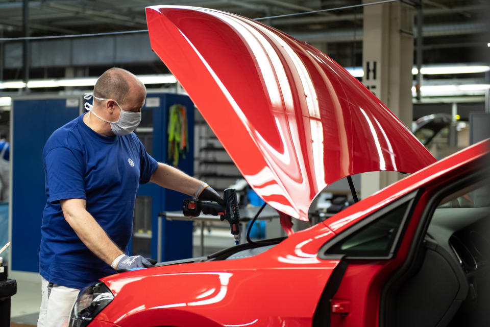 Ein VW-Mitarbeiter mit einem Mund- und Nasenschutz arbeitet in der Produktion an einem Auto im Werk in Wolfsburg (Bild: Swen Pförtner/dpa)