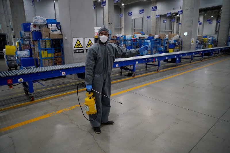 A worker in a protective gear sanitizes packages before leaving to deliver them in Incheon