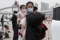 In this Thursday, April 2, 2020, photo, a woman holding a child walks away from the expressway gate at the border of Wuhan city in central China's Hubei province. Millions of Chinese workers are streaming back to factories, shops and offices but many still face anti-coronavirus controls that add to their financial losses and aggravation. In Wuhan police require a health check and documents from employers for returning workers. (AP Photo/Ng Han Guan)