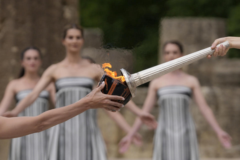 Actress Mary Mina, playing high priestess, right, lights a torch during the official ceremony of the flame lighting for the Paris Olympics, at the Ancient Olympia site, Greece, Tuesday, April 16, 2024. The flame will be carried through Greece for 11 days before being handed over to Paris organizers on April 26. (AP Photo/Thanassis Stavrakis)