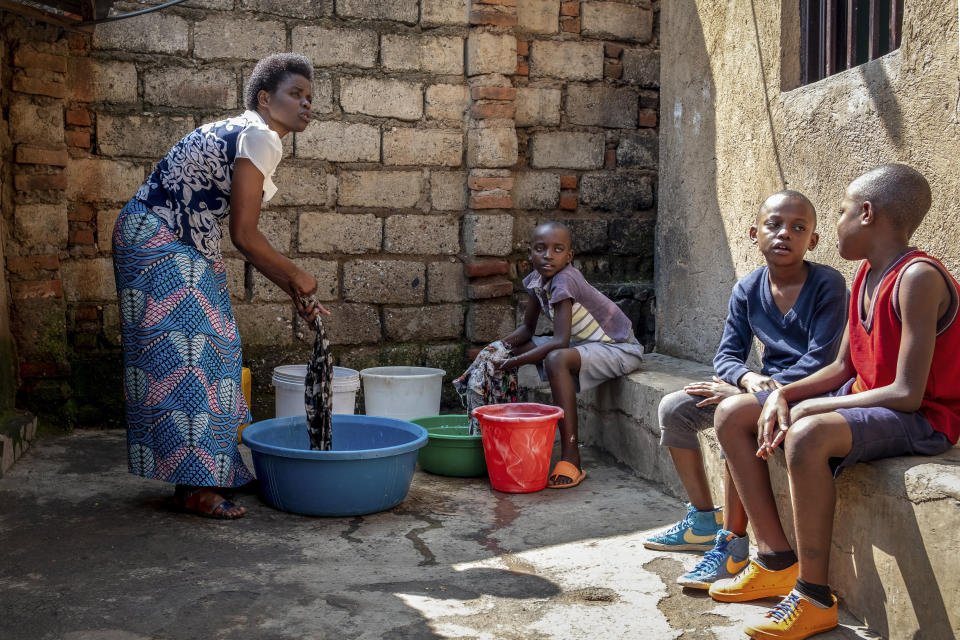 En esta imagen, tomada el 21 de abril de 2020, Tresor Ndizihiwe, de 12 años (centro), ayuda a lavar la ropa a su madre, Jacqueline Mukantwari (izquierda), junto a sus hermanos, en su casa en Kigali, Ruanda. Mukantwari recibía un salario de 50 dólares mensuales como maestra de escuela, pero solía ganar dinero extra al dar clases privadas. Ese negocio se ha terminado y la familia recibe paquetes de alimentos de parte del gobierno dos veces al mes. (AP Foto)