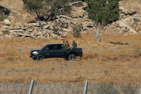 Uniformed men ride a pick-up truck as they carry a Syrian flag in Quneitra on the Syrian side of the ceasefire line between Israel and Syria, as seen from the Israeli-occupied Golan Heights, July 26, 2018. REUTERS/Ammar Awad