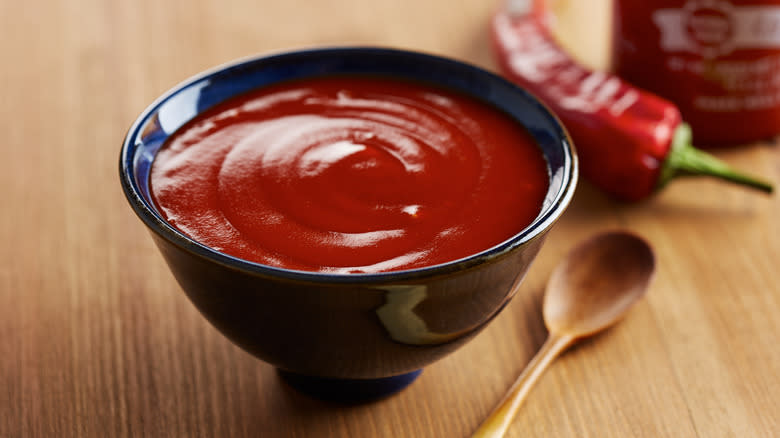 Bowl of sriracha with red jalapeño pepper and spoon