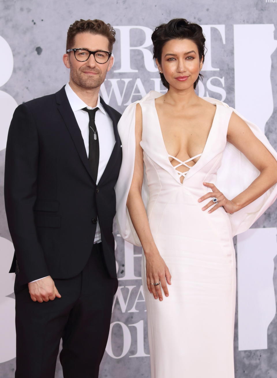 Matthew, in a suit and tie and eyeglasses, and Renee, in a low-cut sleeveless gown, on the red carpet