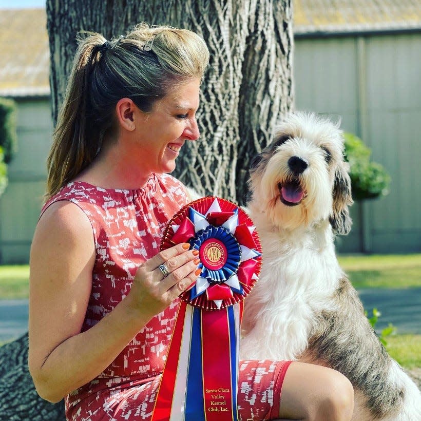 Janice Hayes and her show dog, Buddy Holly, pose with a ribbon Buddy earned at a recent competition.