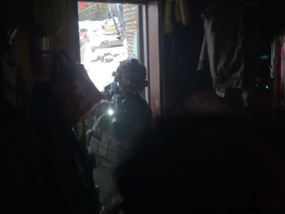 An RCMP tactical officer points his weapon inside a cabin after the door was smashed by an axe and cut with a chainsaw at a blockade of a Coastal GasLink pipeline construction site in northern B.C. on Nov. 19. Police say the authority to enter came from a B.C. Supreme Court injunction issued in 2019. (Courtesy of Yintah Film - image credit)