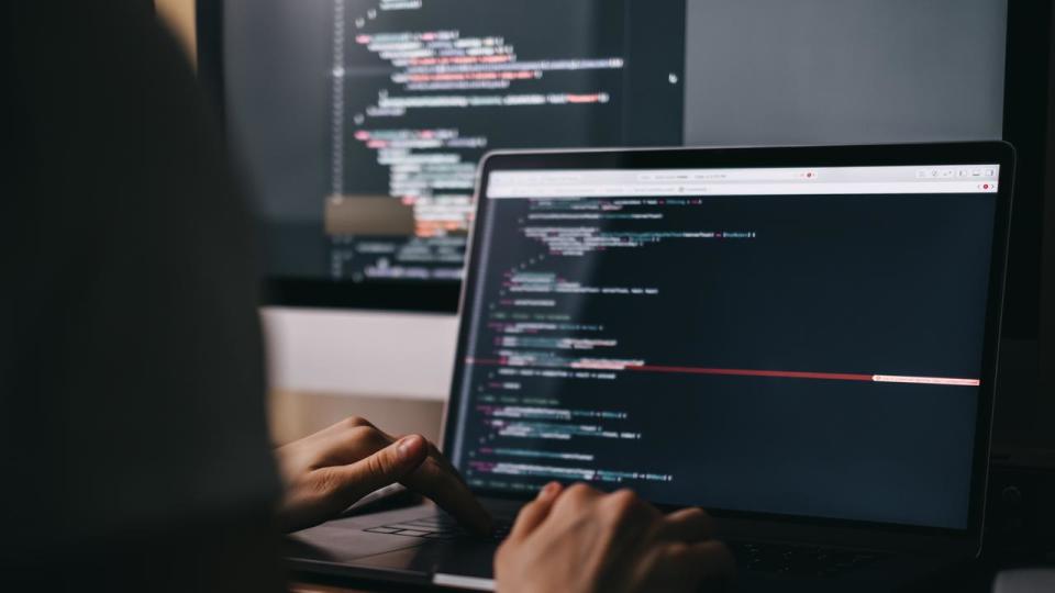 Young caucasian female programmer in glasses writes program code on a laptop