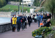People wearing masks to protect against coronavirus, walk, near the Atlantic Ocean in Saint Jean de Luz, southwestern France, Saturday Oct. 17, 2020. France became the latest European country to toughen anti-coronavirus measures, imposing a curfew in Paris and eight other cities from Saturday. (AP Photo/Bob Edme)