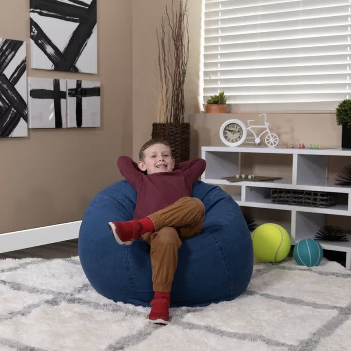 Child model relaxing in the blue bean bag with leg crossed and arms behind head as they lean back