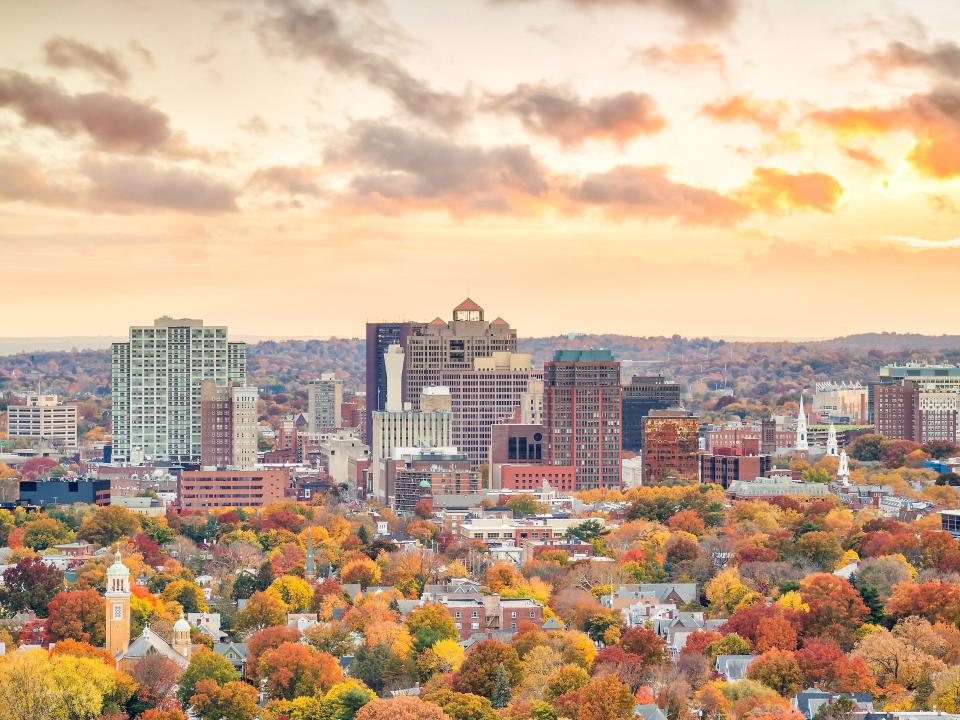 Downtown New Haven, Connecticut, during fall. The trees are varying shades of green, orange, yellow, and red. The sky has an orange tint, too.