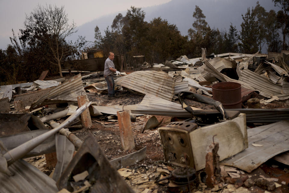 Julio Escobar works on cleaning the debris of his house, that was destroyed by wildfires, in Tome, Chile, Saturday, Feb. 4, 2023. Forest fires are spreading in southern and central Chile, triggering evacuations and the declaration of a state of emergency in some regions. (AP Photo/Matias Delacroix)