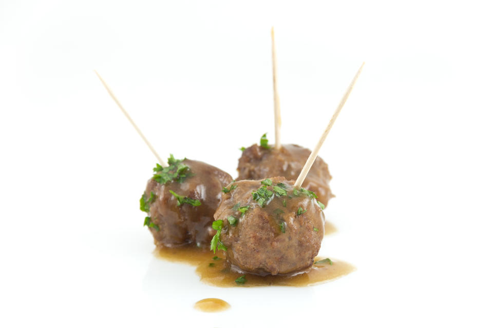 Three meatballs with toothpicks, garnished with herbs and served with sauce on a white background