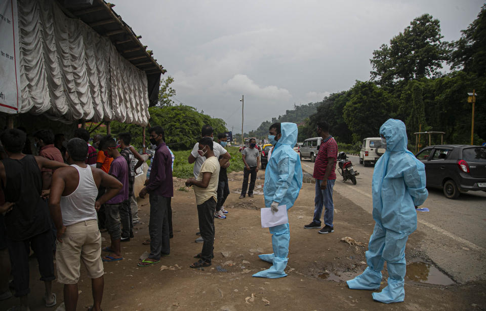 Health workers in protective gear stand in queue with others to get entry passes to travel back to neighboring Meghalaya state as they return after bringing a COVID-19 patient in Gauhati, India, Sunday, Aug. 9, 2020. Interstate travel is restricted due to the pandemic. (AP Photo/Anupam Nath)