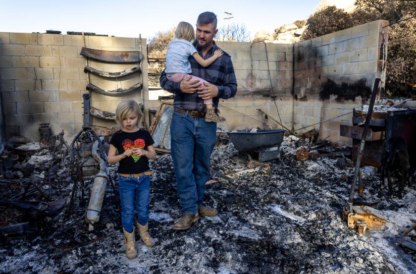 AGUANGA, CA - NOVEMBER 22, 2023: Single dad Cody McCormick with his two daughters Allison, 4, and Kayla,6, walk through parts of their destroyed garage which was reduced to ashes along with they home after the October Highland fire swept through on November 22, 2023 in Aguanga, California. He and the girls are staying in a borrowed trailer on the adjacent property. (Gina Ferazzi / Los Angeles Times)