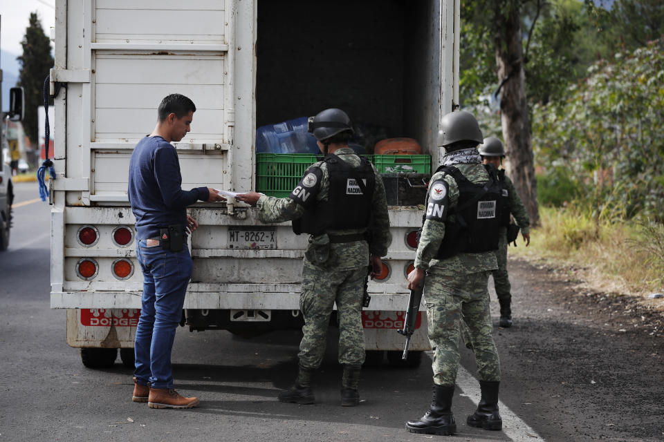 In this Feb. 6, 2020 photo, National Guards work a checkpoint leading into Uruapan, Michoacan state, Mexico. Uruapan, a city of about 340,000 people, is in Mexico's avocado belt, where violence has reached shocking proportions. In Uruapan, cartels are battling for territory and reports of killings are common, such as the gun massacre last week of three young boys, a teenager and five others at an arcade in what had been a relatively quiet neighborhood. (AP Photo/Marco Ugarte)