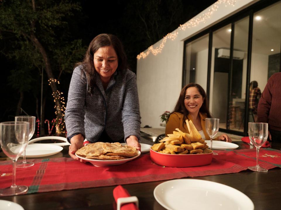 a happy latin grandmother putting christmas food on a table outside home and smiling