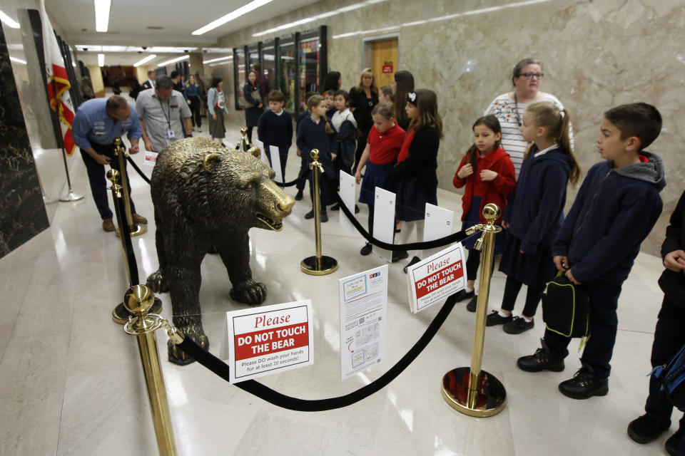 Children view the sculpture of a bear outside the office of Gov. Gavin Newsom at the Capitol in Sacramento, Calif., Thursday, March 12, 2020. In another coronavirus precaution, California officials cordoned off the sculpture, that was purchased by former governor Arnold Schwarzenegger, and was quickly nicknamed "Bacteria Bear" after it became a favorite backdrop for photographs and selfies by school children and other Capitol visitors. (AP Photo/Rich Pedroncelli)