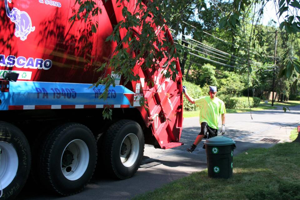 An employee of J.P. Mascaro & Sons prepares to empty a can of recyclables into a disposal truck.  Mascaro and other trash haulers have had issues with hiring employees since the pandemic started last year.