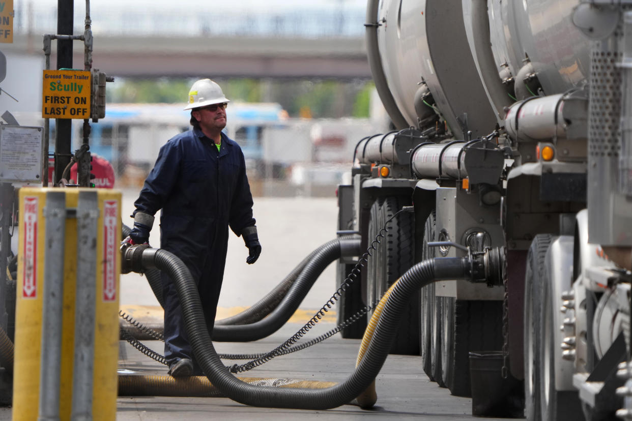 A driver in overalls and hardhat adjusts a spigot on a huge pipe as he unloads raw crude oil from his tanker.