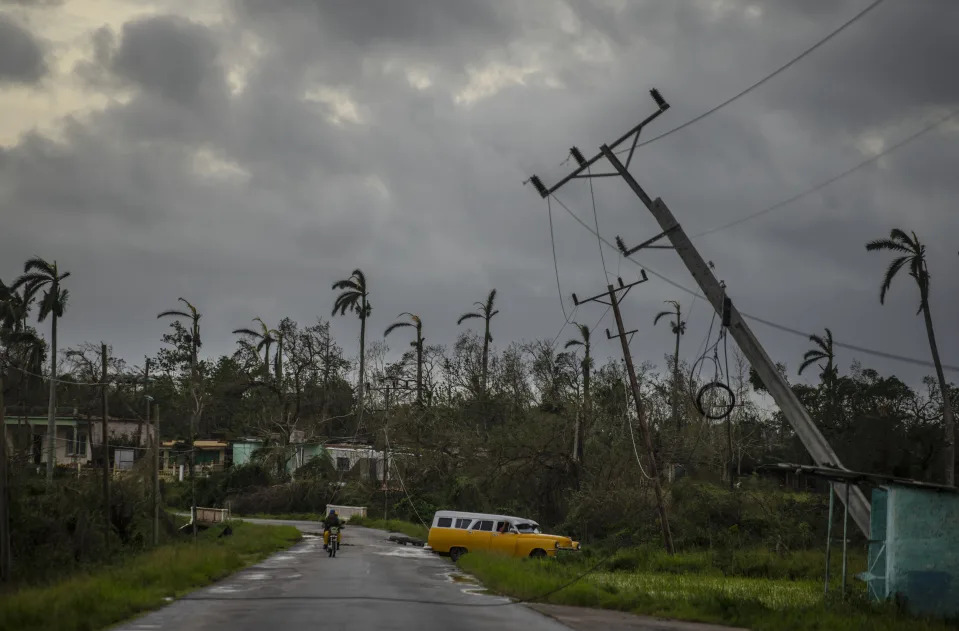 A classic American car drives past utility poles tilted by Hurricane Ian in Pinar del Rio, Cuba, Tuesday, Sept. 27, 2022. (AP Photo/Ramon Espinosa)