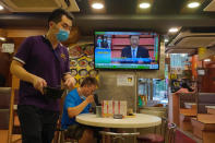 A man has lunch beneath a television showing live telecast of Chinese President Xi Jinping at the closing session of the National People's Congress, in Hong Kong, Thursday, May 28, 2020. China’s ceremonial legislature on Thursday endorsed a national security law for Hong Kong that has strained relations with the United States and Britain. (AP Photo/Vincent Yu)