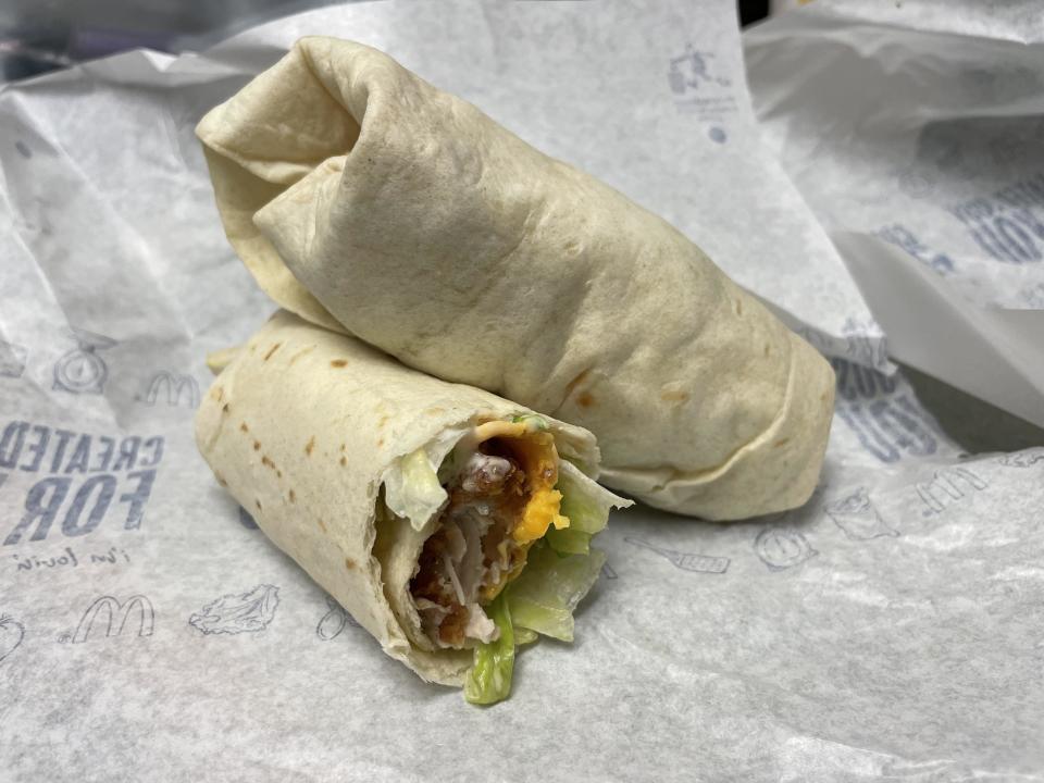 A cut burrito with visible ingredients such as lettuce, bacon, and cheese sits on McDonald's branded paper