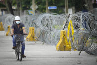 A men cycling next to coils of barbed wire near Top Glove factory hostel in Shah Alam, Malaysia, Wednesday, Nov. 25, 2020. Malaysia's Top Glove Corp., the world's largest maker of rubber gloves, says it expects a two to four-week delay in deliveries after more than 2,000 workers at its factories were infected by the coronavirus, raising the possibility of supply disruptions during the pandemic. (AP Photo/Vincent Thian)