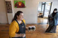 Cafe owner Maria Iatrou, left, serves take-away coffee to customers in Melbourne, Monday, July 6, 2020. As Australia is emerging from pandemic restrictions, the Victoria state capital Melbourne is buckling down with more extreme and divisive measures that are causing anger and igniting arguments over who is to blame as the disease spreads again at an alarming rate. (AP Photo/Andy Brownbill)