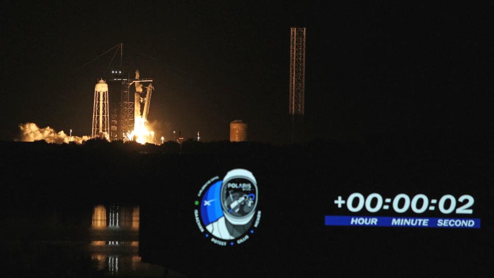 a white rocket lifts off at night above a plume of fire and smoke