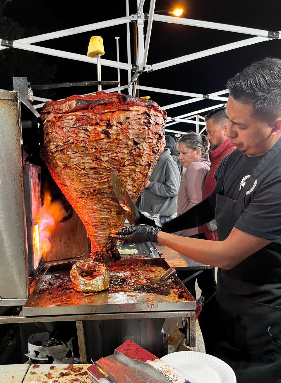A worker at a sidewalk taco stand in Ventura shaves pork prepared al pastor, from the spit on March 25.
