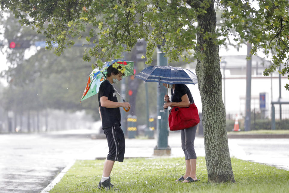 Keller Bell, left, and his mother Sheri Bell shelter from the rain under a tree and umbrellas as they wait for a bus in advance of Tropical Storm Cristobal in New Orleans, Sunday, June 7, 2020. (AP Photo/Gerald Herbert)